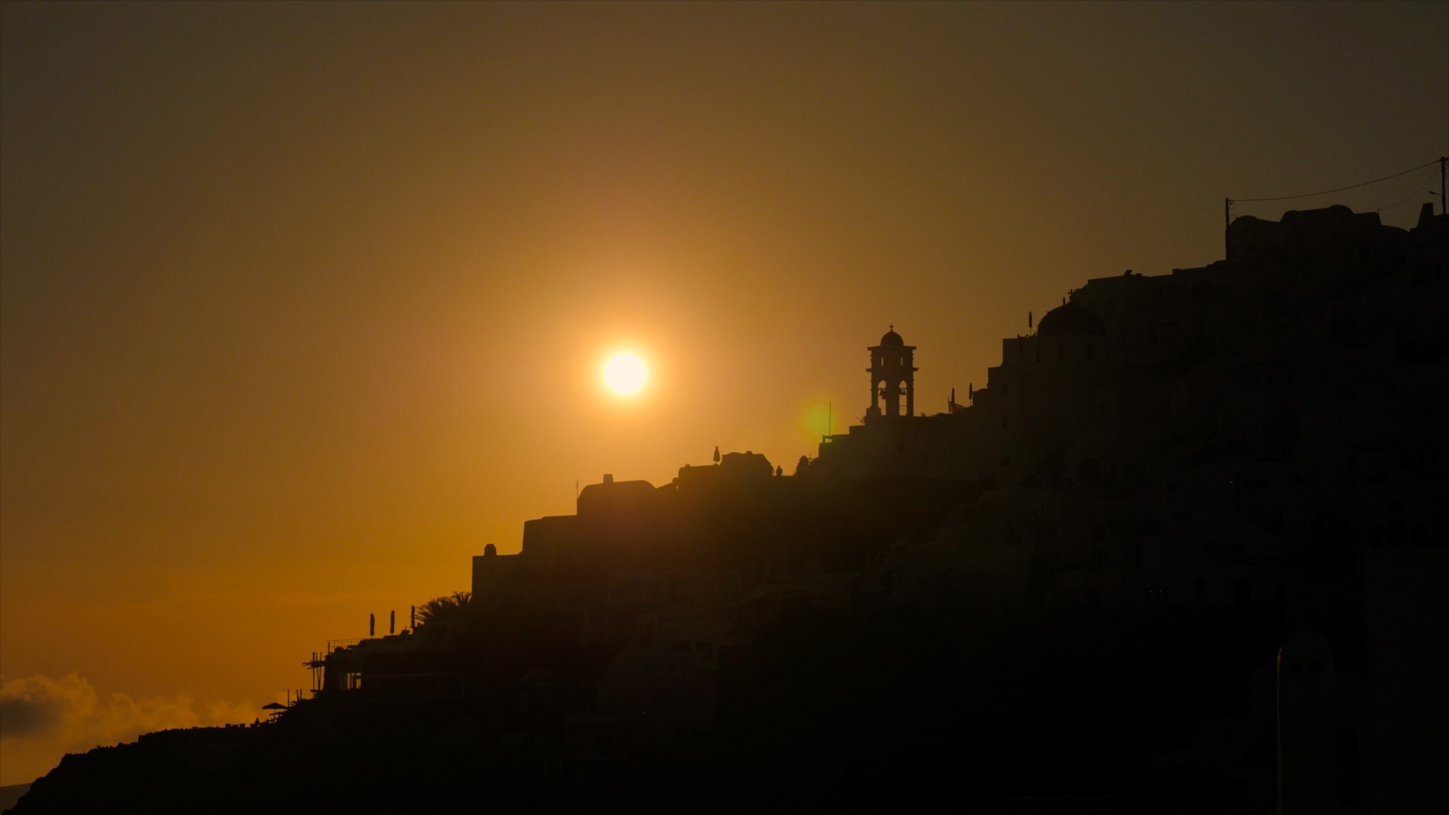 The sun falls behind the mountains in Santorini, Greece.