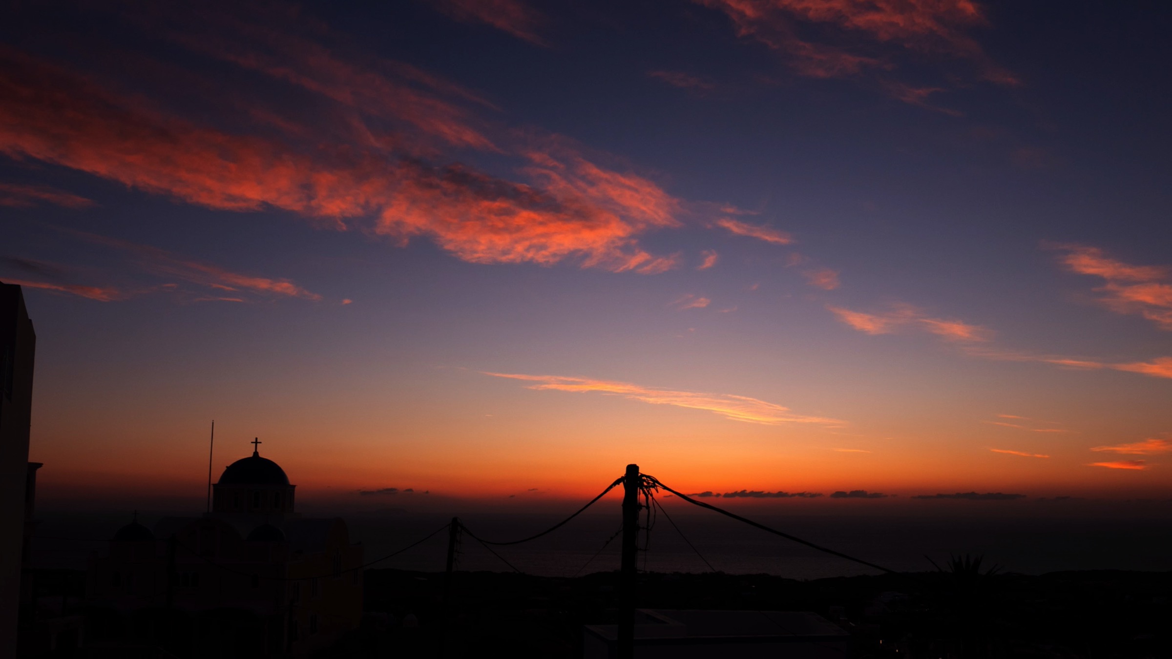 A beautiful sunrise with orange, pink and blue hues flowing over the silhouetted skyline of Santorini.
