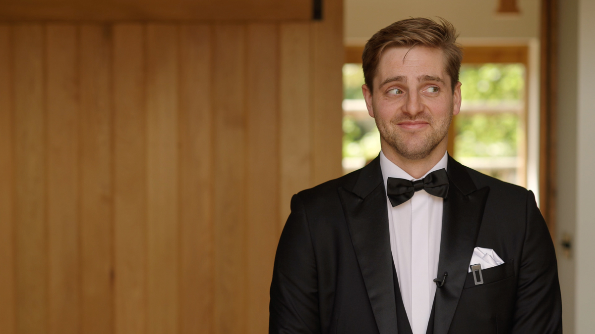 The groom stands with his back to the door, where his bride is about to see him for the first time.